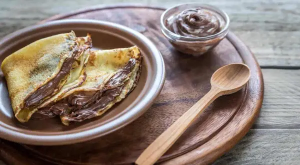Crepes ripiene di una golosa nutella fatta in casa, pronte per essere gustate con un cucchiaino di legno.