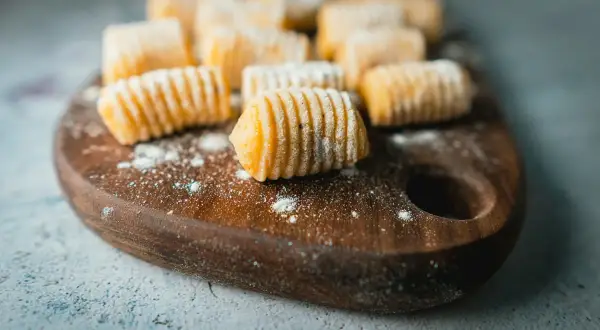 Gnocchi fatti in casa, pronti per la cottura. La **gnocchi ricetta perfetta** è a portata di mano su un tagliere di legno.