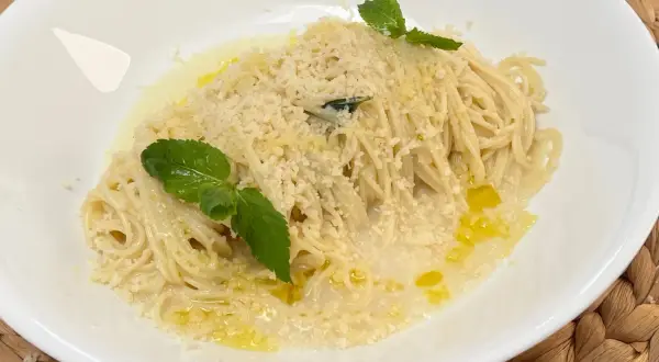 Spaghetti al limone cremosi, conditi con parmigiano e guarniti con menta fresca. Un piatto invitante e profumato.