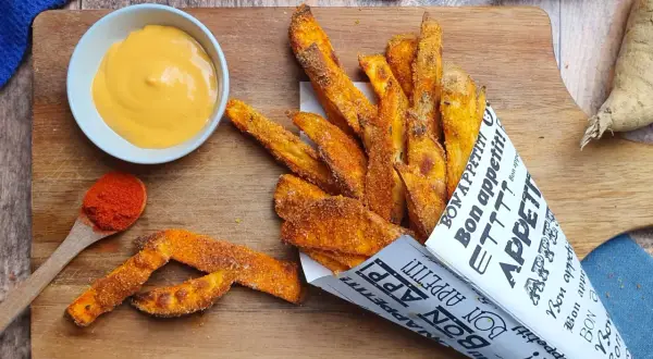 Patate dolci fritte croccanti, servite in un cono di carta con la scritta "Bon appétit!", accompagnate da una salsa cremosa e paprika.