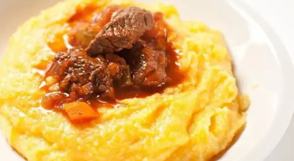 Un invitante spezzatino con piselli, servito su un letto di morbida polenta gialla. Un piatto confortante e saporito.