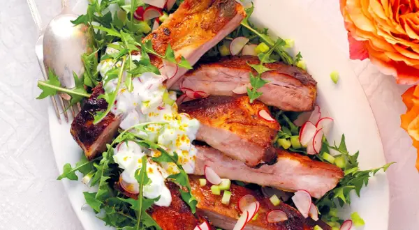 Costine di maiale succulente, perfette per una marinatura saporita, servite su un letto di rucola e ravanelli, con una salsa cremosa.