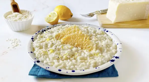 Un cremoso riso al limone freddo, guarnito con scorza di limone e parmigiano grattugiato, pronto per essere gustato.