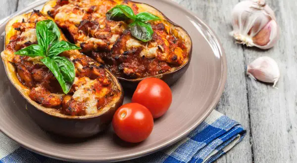Melanzane alla siciliana, gustoso piatto con melanzane ripiene, pomodorini e basilico fresco, su un tavolo di legno.