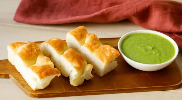 Focaccia tagliata a pezzi su tagliere di legno, accanto una ciotolina con pesto di salvia.