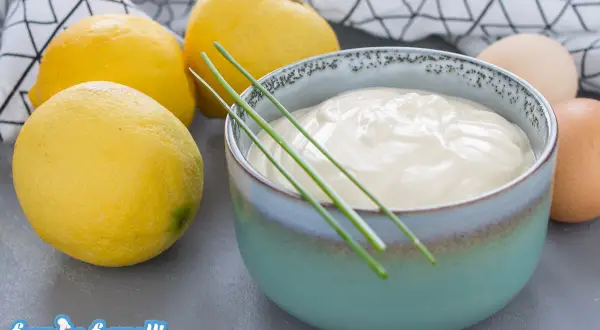 Una ciotola di cremosa maionese allo yogurt, guarnita con erba cipollina, accanto a limoni freschi e uova.