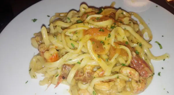 Un piatto invitante di tagliolini agli scampi, con pasta fresca e succulenti crostacei in una cremosa salsa, guarnito con prezzemolo tritato.