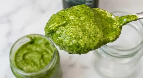 Un cucchiaio pieno di pesto fatto in casa, verde brillante, pronto per essere gustato.