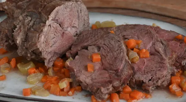 Arrosto di vitello morbido con sughetto e verdure. La carne è succulenta e tagliata a fette, immersa in un delizioso sughetto con carote e sedano a cubetti.