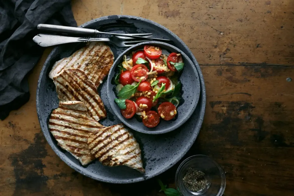 Delizioso paillard di vitello grigliato servito con un'insalata fresca di pomodorini, basilico e pinoli.
