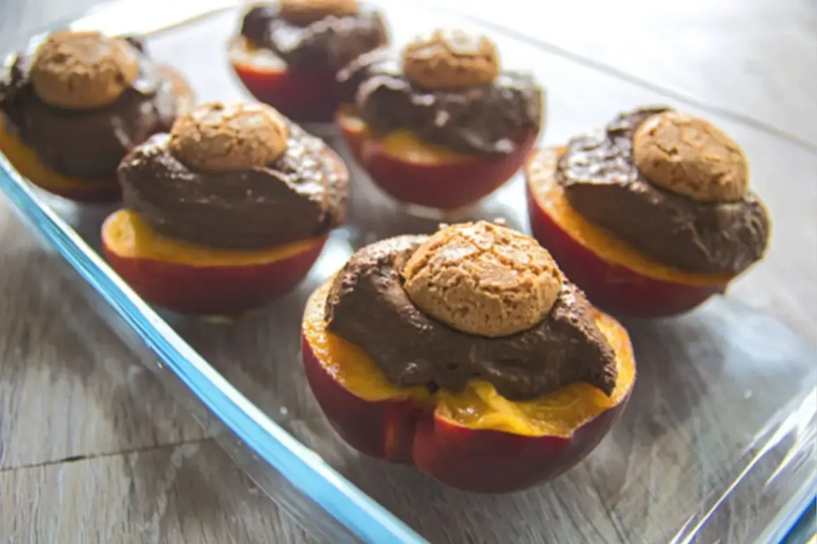 Pesche al forno con amaretti: dolci metà di pesche rosse ripiene di crema al cioccolato e guarnite con un amaretto croccante.