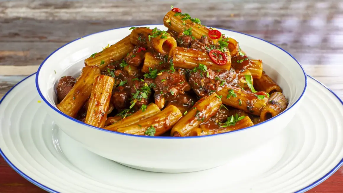 Rigatoni conditi con un saporito ragù di polpo, guarniti con prezzemolo fresco e peperoncino.
