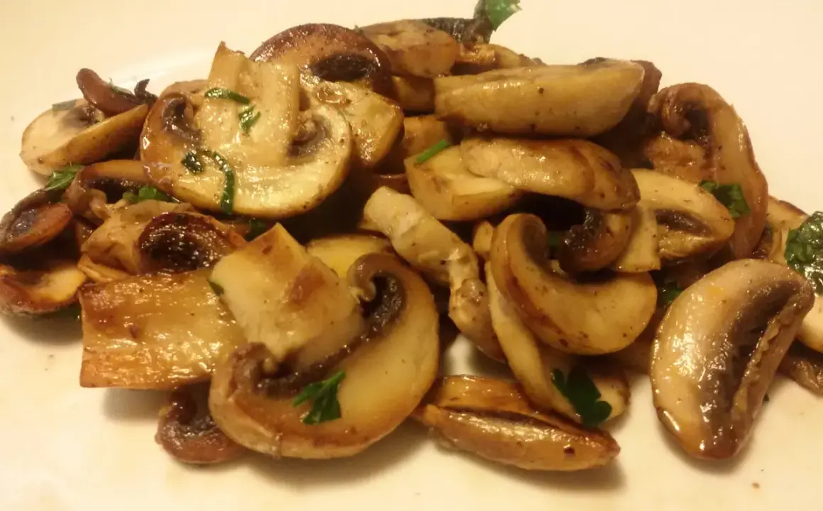 Funghi champignon in padella, dorati e succulenti, guarniti con prezzemolo fresco. Un contorno semplice e gustoso.