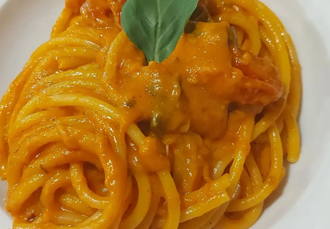 Un piatto invitante di pasta con i pomodorini, condita con una salsa cremosa e guarnita con una foglia di basilico fresco.