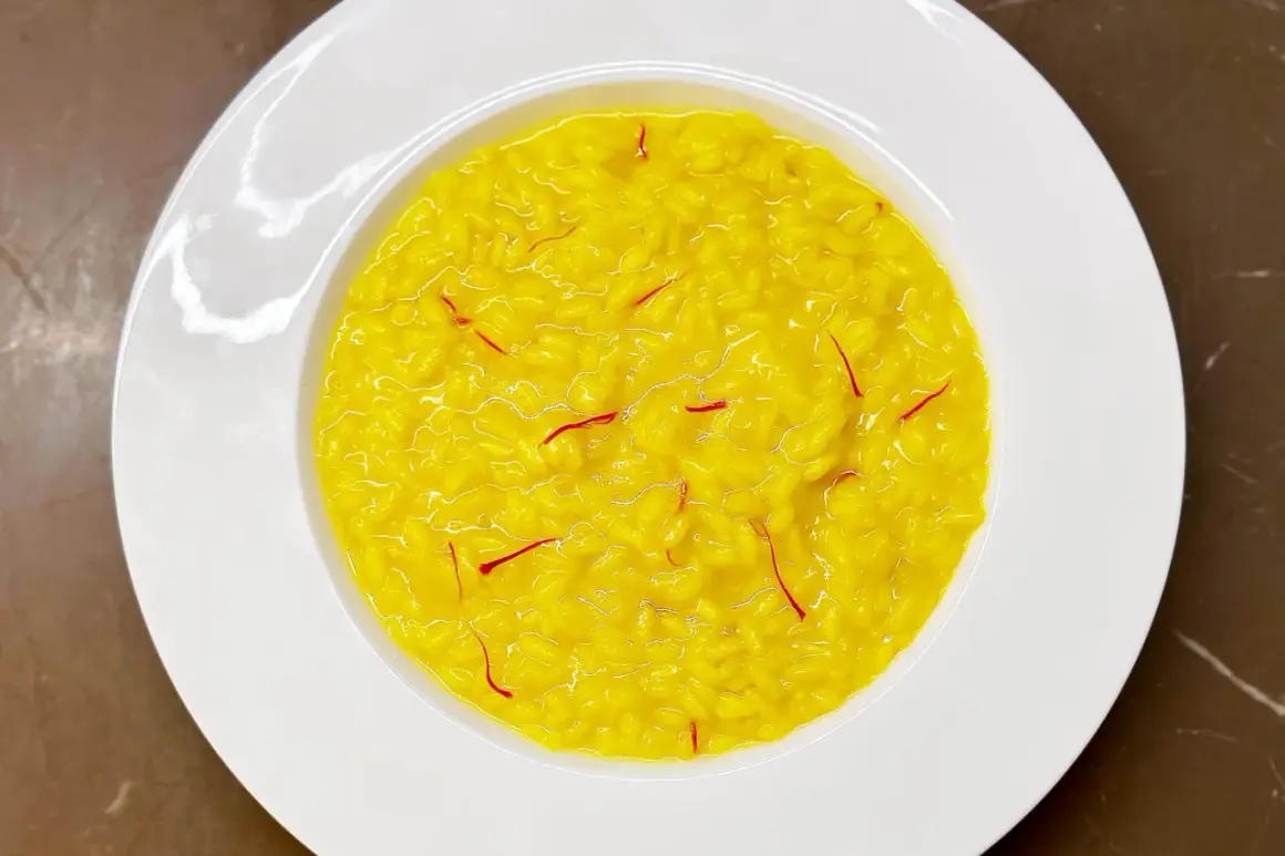 Un cremoso risotto alla milanese, giallo intenso con fili di zafferano, servito in un piatto bianco.