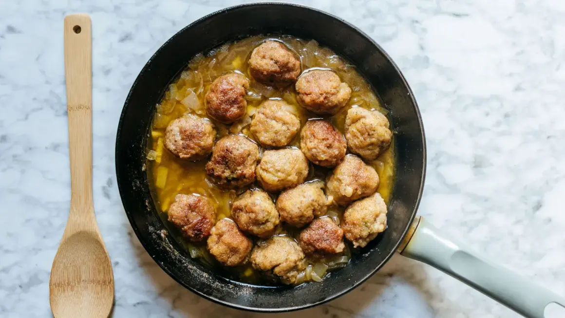 Polpette in bianco cremose in padella, dorate e succulente, pronte per essere gustate con un cucchiaio di legno.