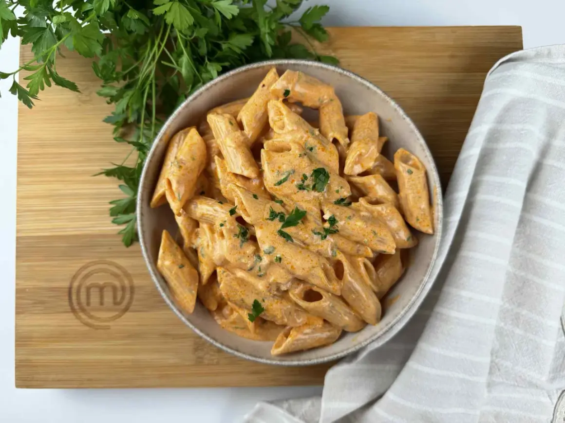 Penne alla vodka cremose e invitanti, guarnite con prezzemolo fresco, su un tagliere di legno con il logo MasterChef.