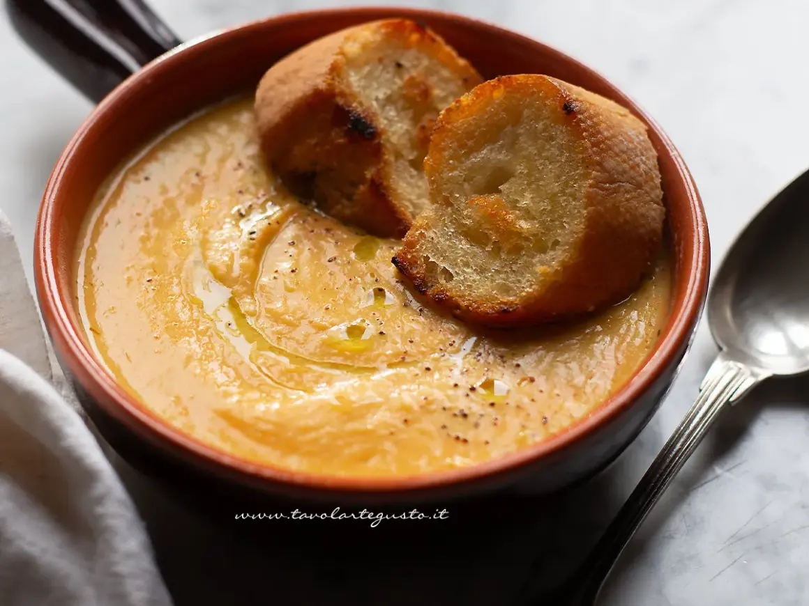 Una ciotola di terracotta con una cremosa zuppa di fagioli, guarnita con crostini dorati e un filo d'olio.