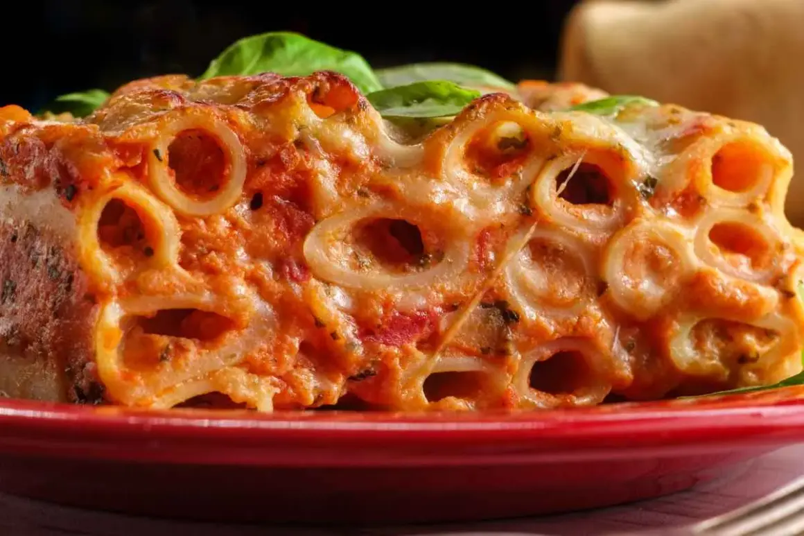 Un primo piatto invitante di ziti al forno, con sugo rosso e formaggio filante, guarnito con foglie di basilico fresco.