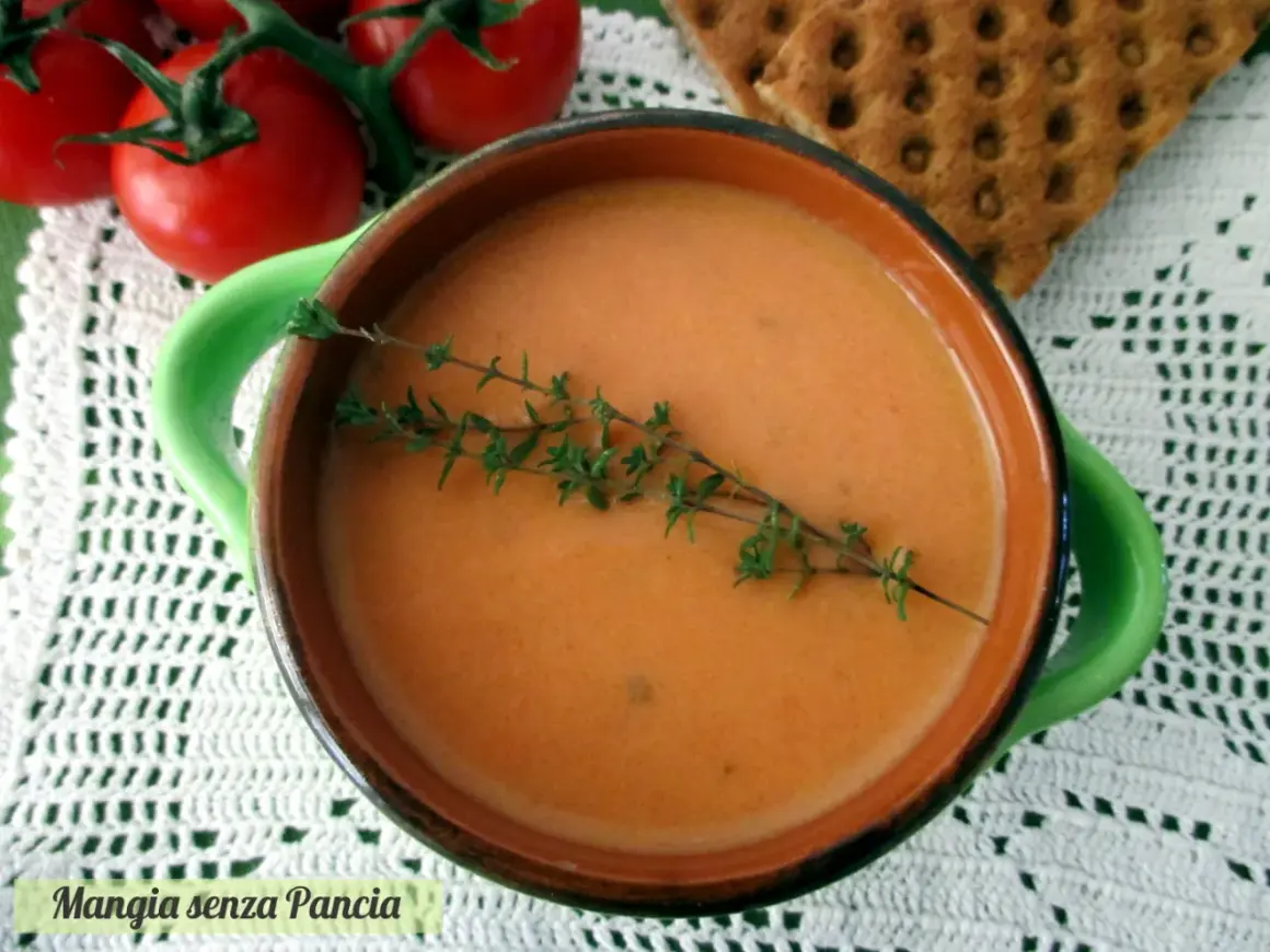 Una ciotola di cremosa crema di pomodoro, guarnita con timo fresco, accanto a pomodori maturi e cracker croccanti.