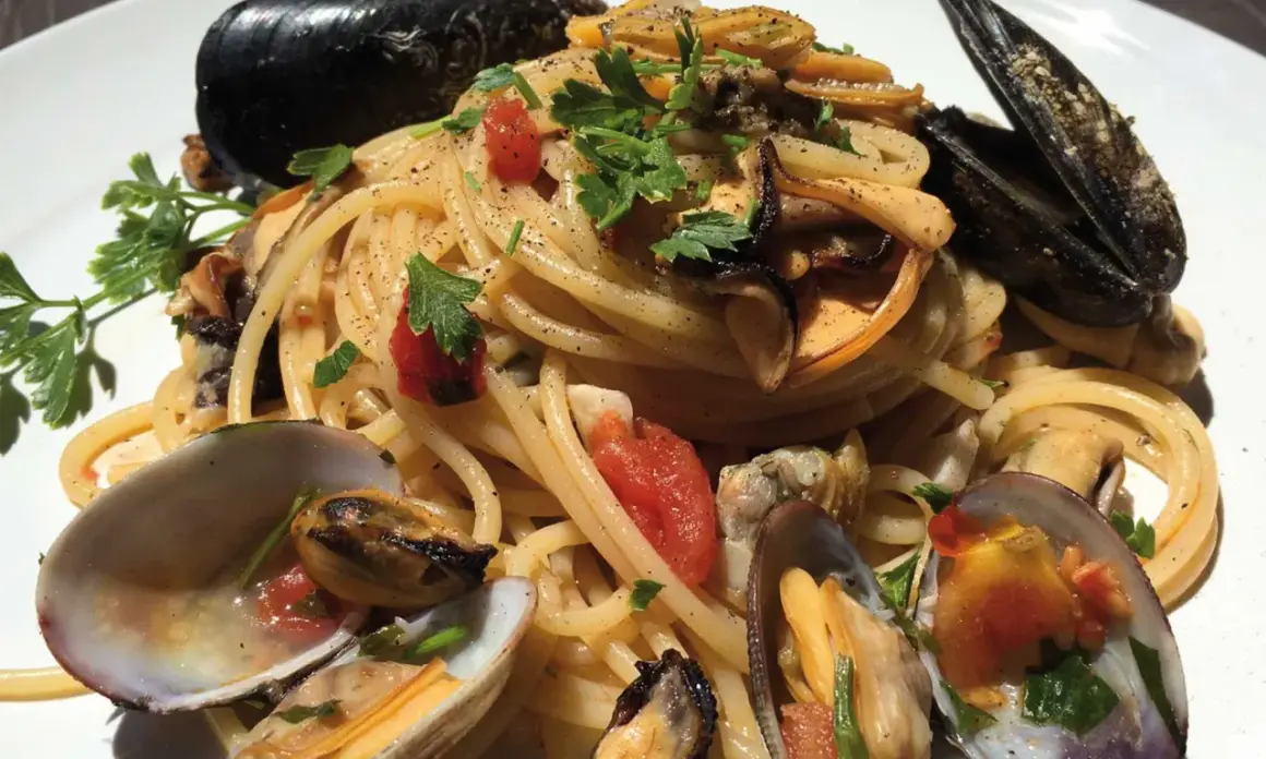 Spaghetti con cozze e vongole, un piatto cremoso e saporito, guarnito con prezzemolo fresco e pomodorini.