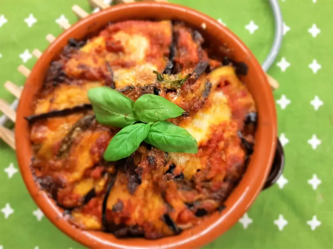 Deliziosa pasta alla norma al forno, con melanzane, pomodoro e basilico fresco, servita in una terrina di terracotta.