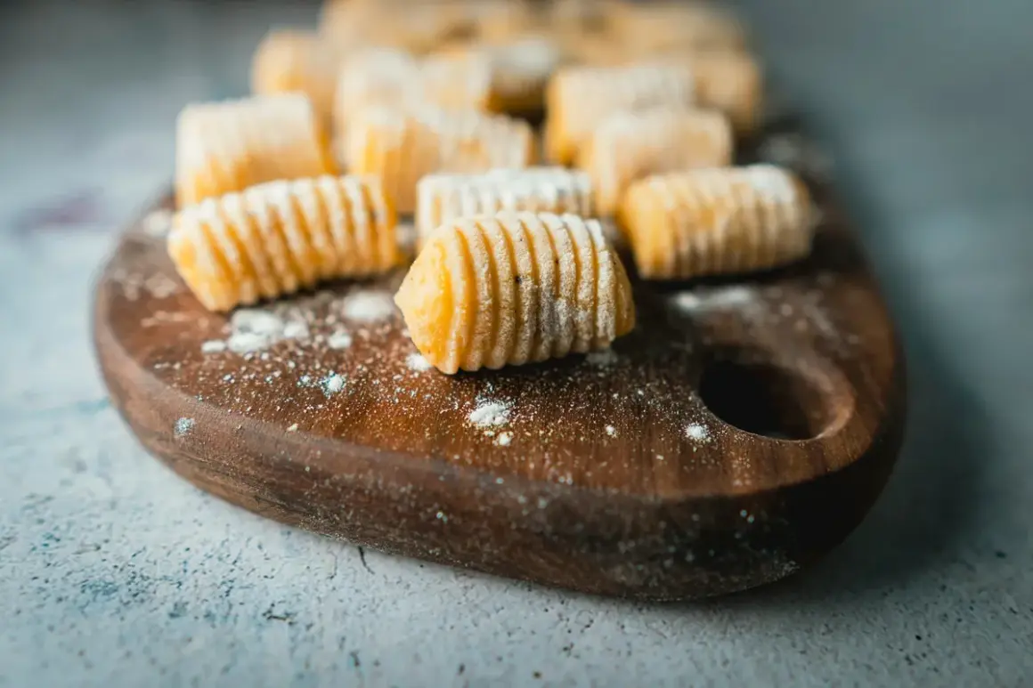 Gnocchi fatti in casa, pronti per la cottura. La **gnocchi ricetta perfetta** è a portata di mano su un tagliere di legno.