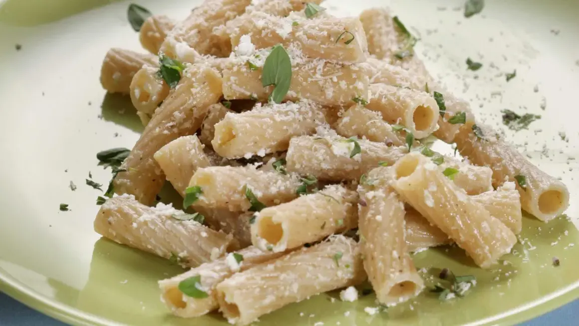 Maccheroni alla pastora conditi con formaggio grattugiato e erbe aromatiche fresche, un piatto semplice e gustoso.