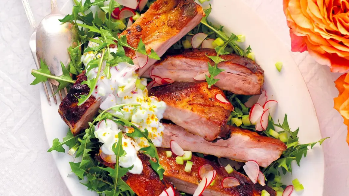 Costine di maiale succulente, perfette per una marinatura saporita, servite su un letto di rucola e ravanelli, con una salsa cremosa.