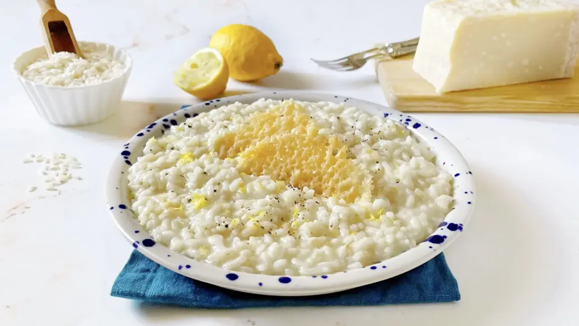Un cremoso riso al limone freddo, guarnito con scorza di limone e parmigiano grattugiato, pronto per essere gustato.