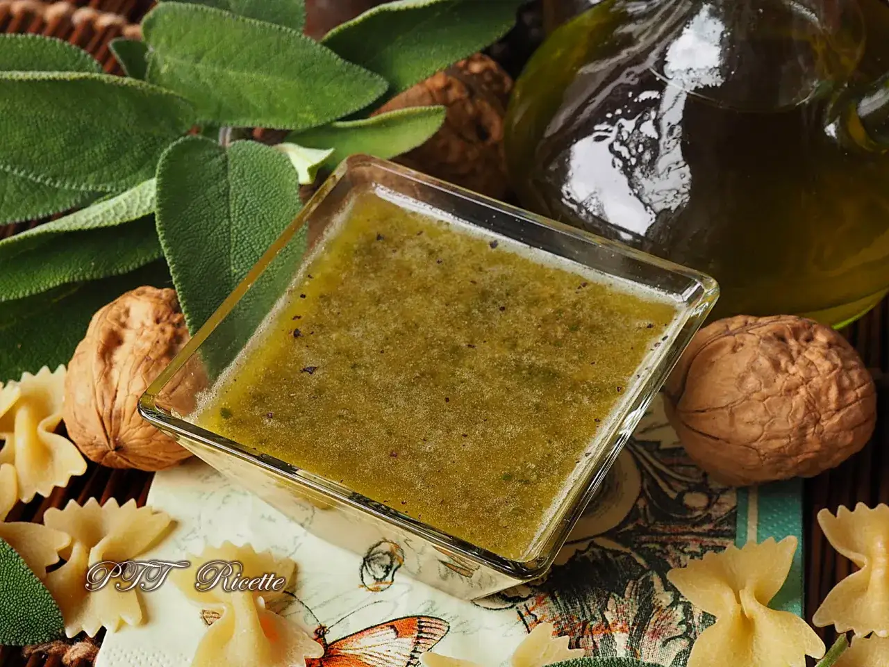 Pesto di salvia in una ciotola di vetro, con noci, foglie di salvia fresca e pasta farfalle.