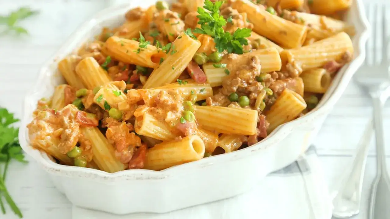 Un piatto invitante di maccheroni alla pastora con ragù cremoso, piselli e pancetta, guarnito con prezzemolo fresco.