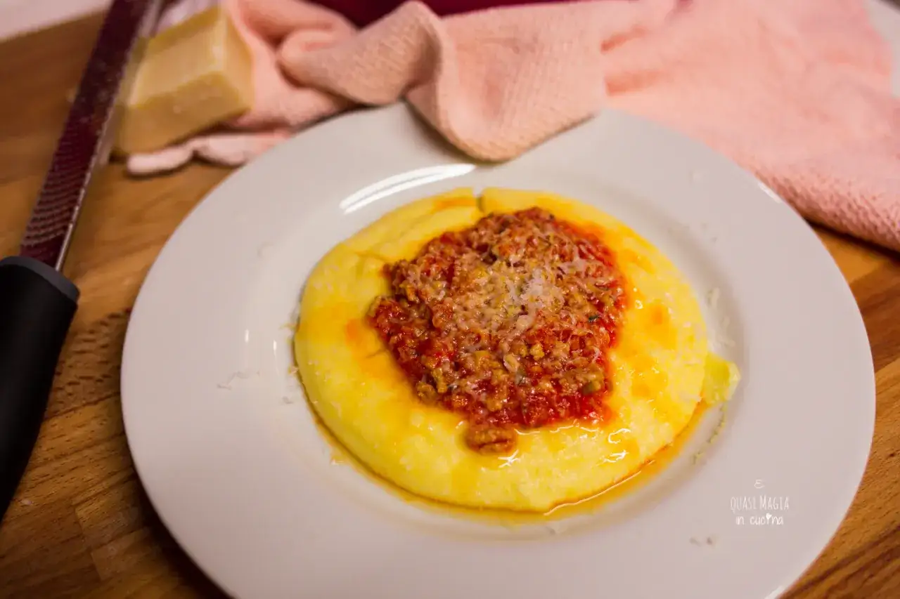 Polenta cremosa con un ricco sugo con salsiccia e parmigiano grattugiato, pronto per essere gustato.