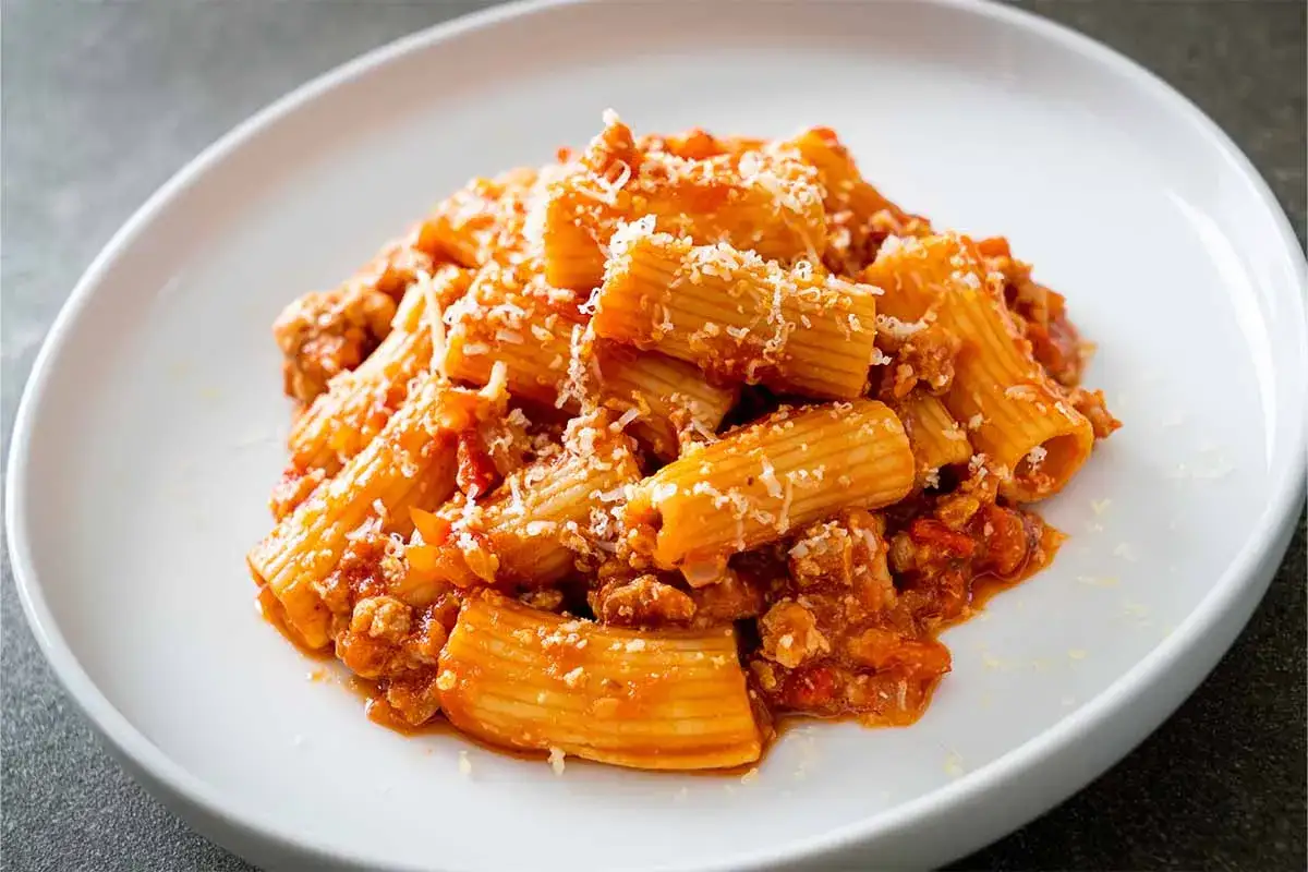 Rigatoni abbondanti conditi con un ricco ragù e abbondante parmigiano, un piatto di pasta alla zozzona che fa venire l'acquolina in bocca.