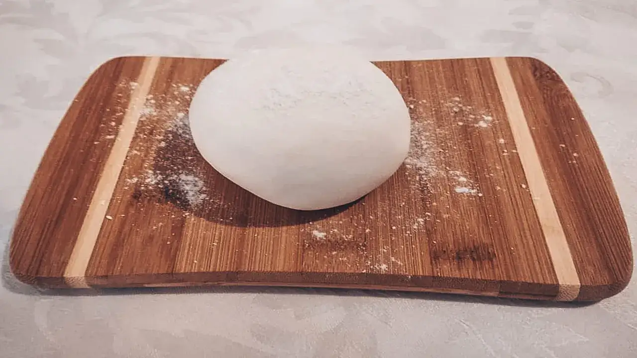 Una palla di pasta di zucchero bianca, soffice e pronta per essere modellata, giace su un tagliere di legno.