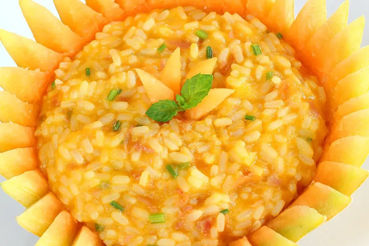 Risotto con melone, un piatto estivo cremoso e colorato, decorato con spicchi di melone e foglioline di menta.