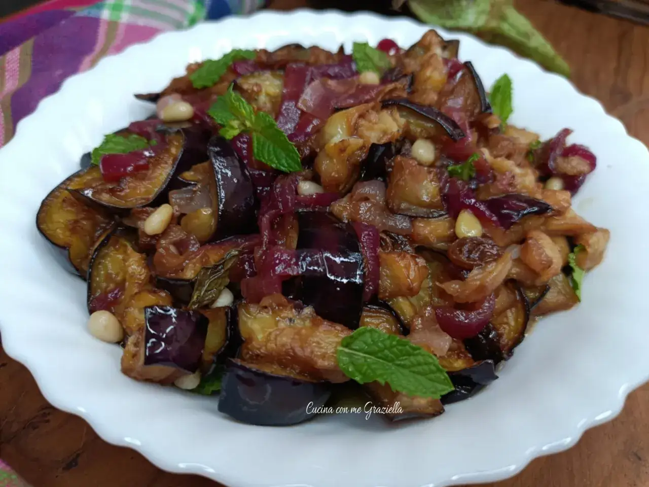 Melanzane in agrodolce, un piatto saporito con cipolle rosse, pinoli e menta fresca.