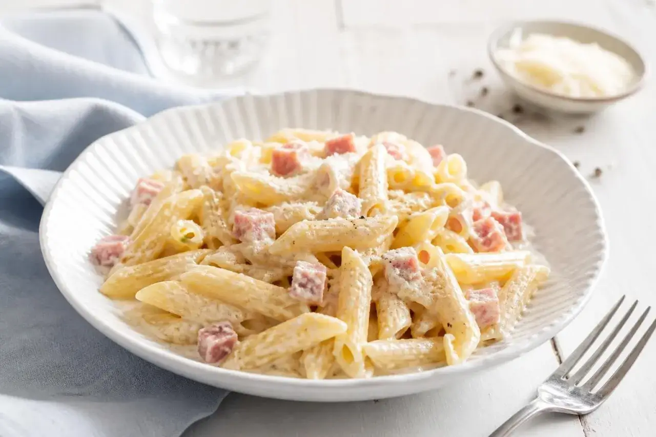 Penne cremose con prosciutto a cubetti, un piatto invitante di pasta panna e prosciutto, spolverato di parmigiano.