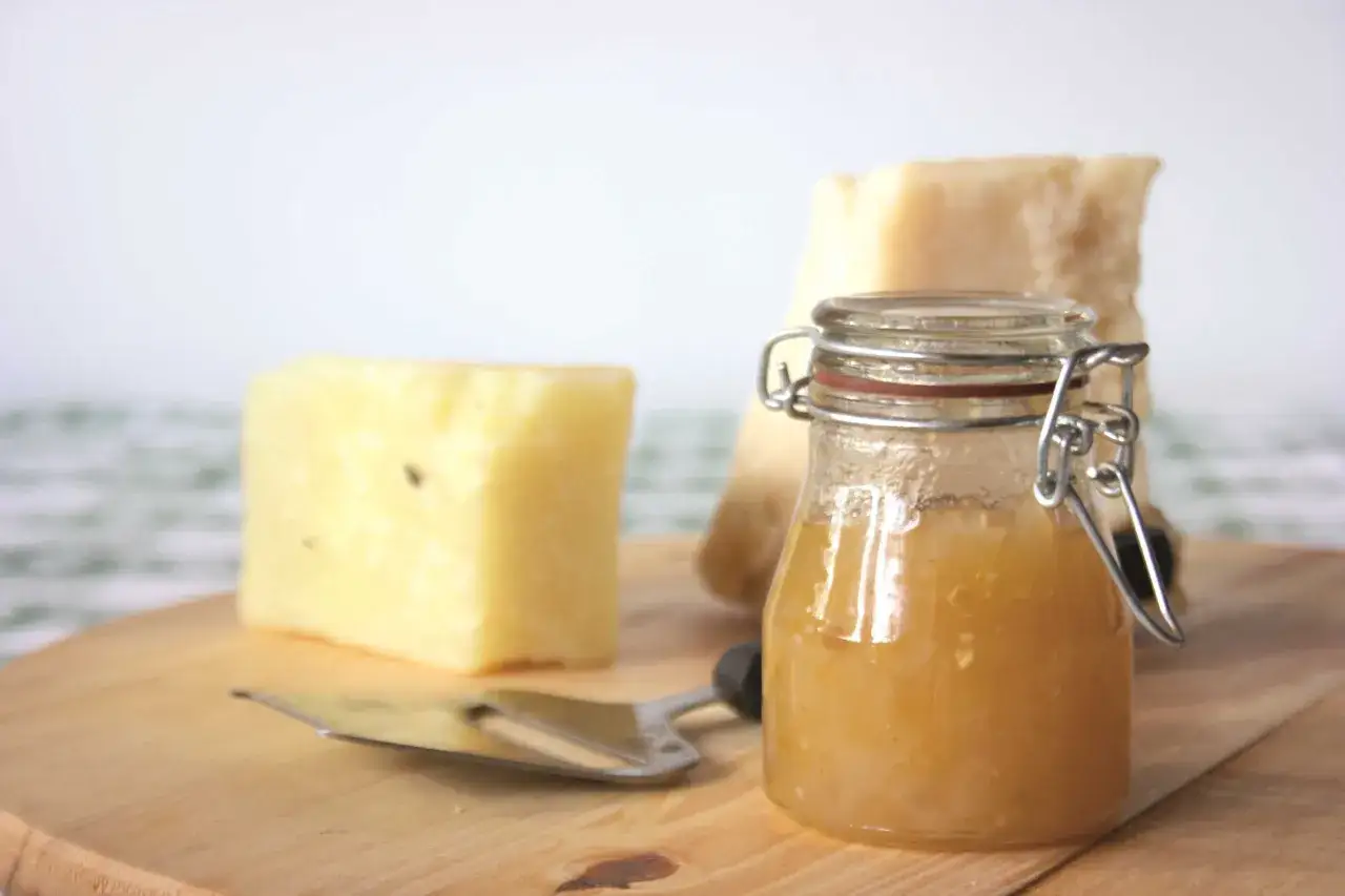 Un vasetto di marmellata di melanzane accanto a due pezzi di formaggio stagionato e un tagliere.