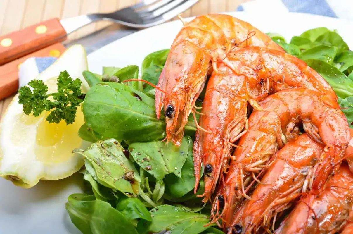 Gamberoni succulenti, pronti per la griglia, con un'insalata fresca e una fetta di limone. La marinatura per gamberoni alla griglia li rende irresistibili.