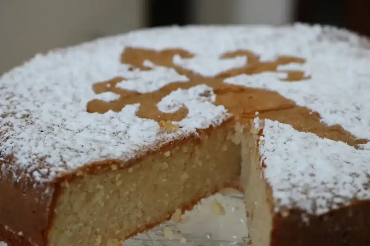 Torta di Santiago cosparsa di zucchero a velo, con un disegno stilizzato di un leone. Una fetta è stata tagliata.