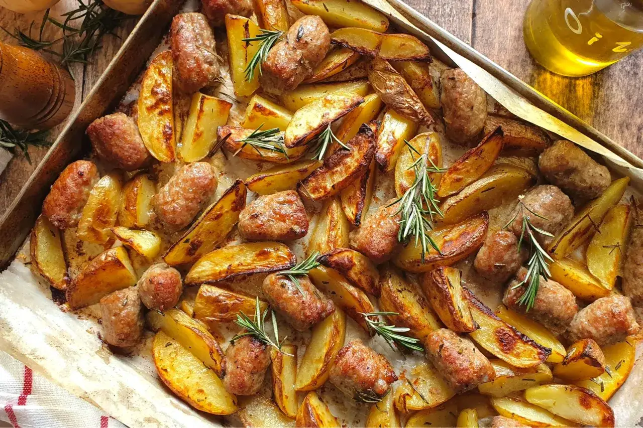 Salsicce e patate al forno, dorate e profumate al rosmarino, pronte per essere gustate.