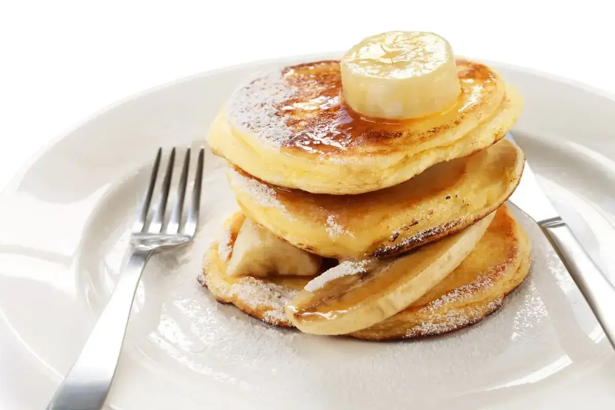 Pancake con albumi soffici, guarniti con fette di banana e sciroppo d'acero, spolverati di zucchero a velo.
