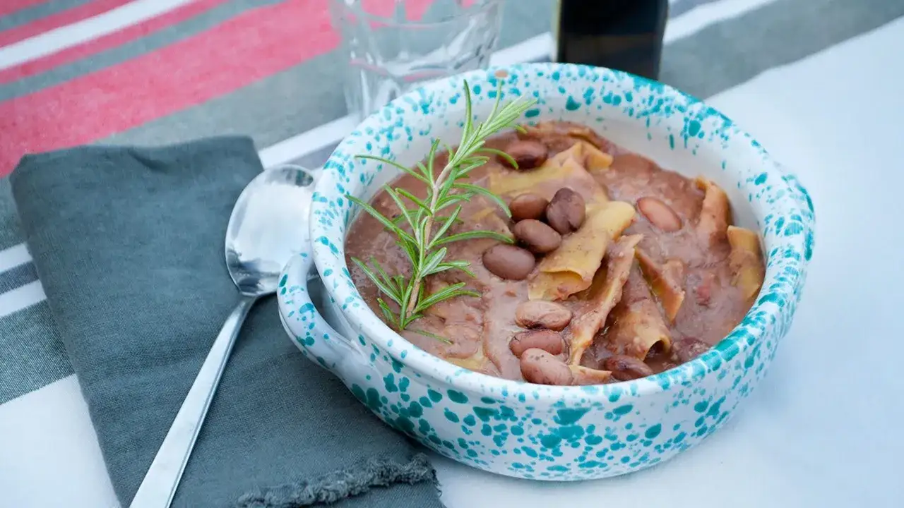 Un piatto invitante di maltagliati con fagioli, guarnito con rosmarino fresco, in una ciotola decorata.
