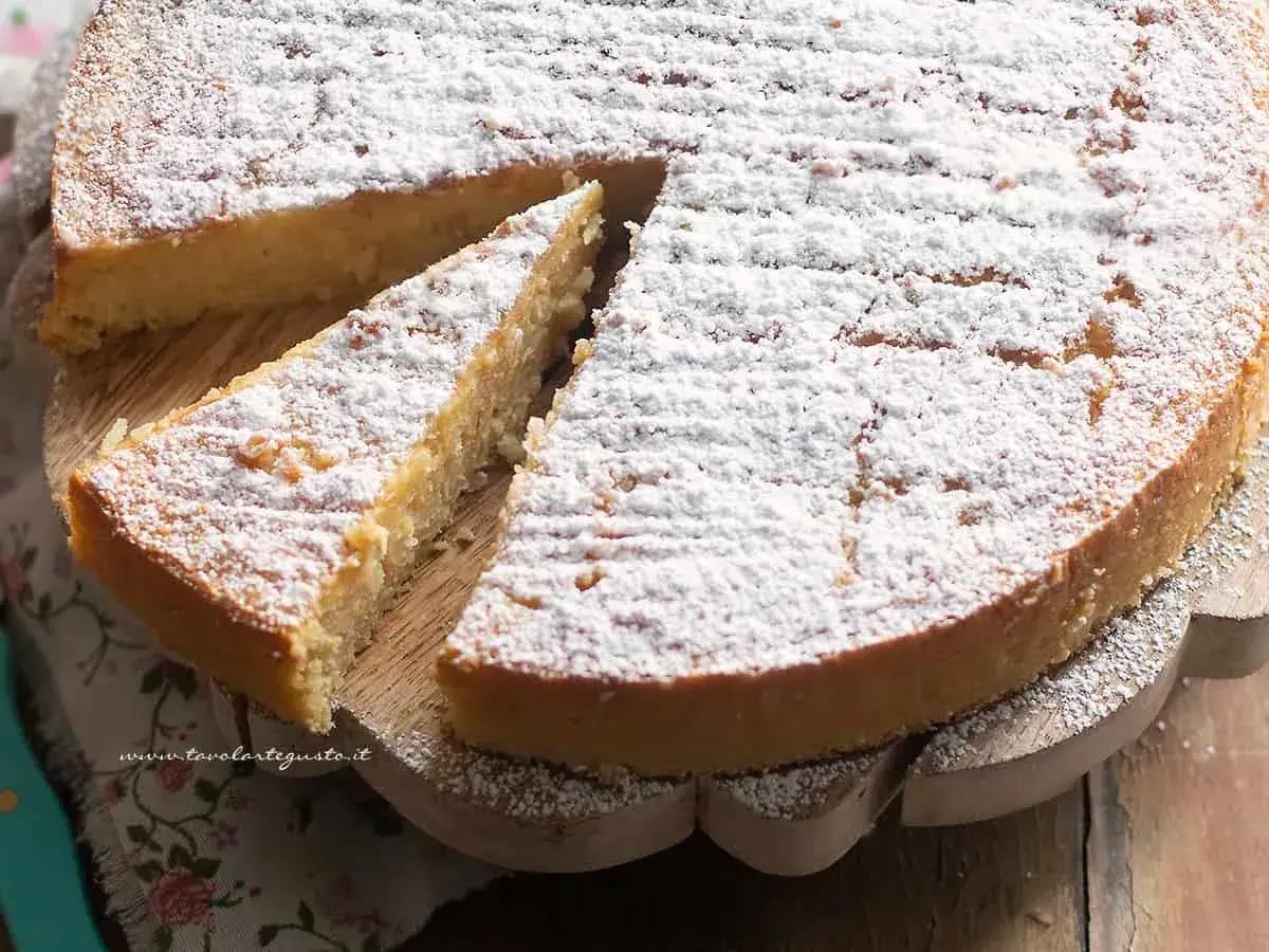 Torta di riso ricetta originale, soffice e profumata, cosparsa di zucchero a velo. Una fetta invitante è già stata tagliata.