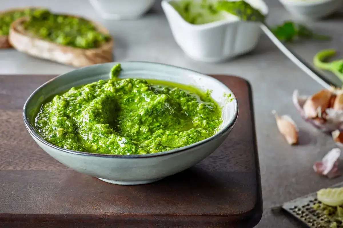 Pesto fatto in casa in una ciotola, con pane tostato e ingredienti freschi sullo sfondo.