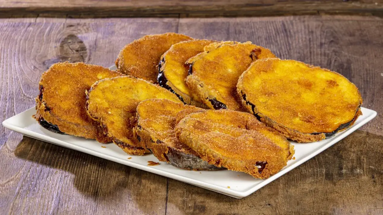 Fette di melanzane fritte solo con farina, dorate e croccanti, servite su un piatto bianco.