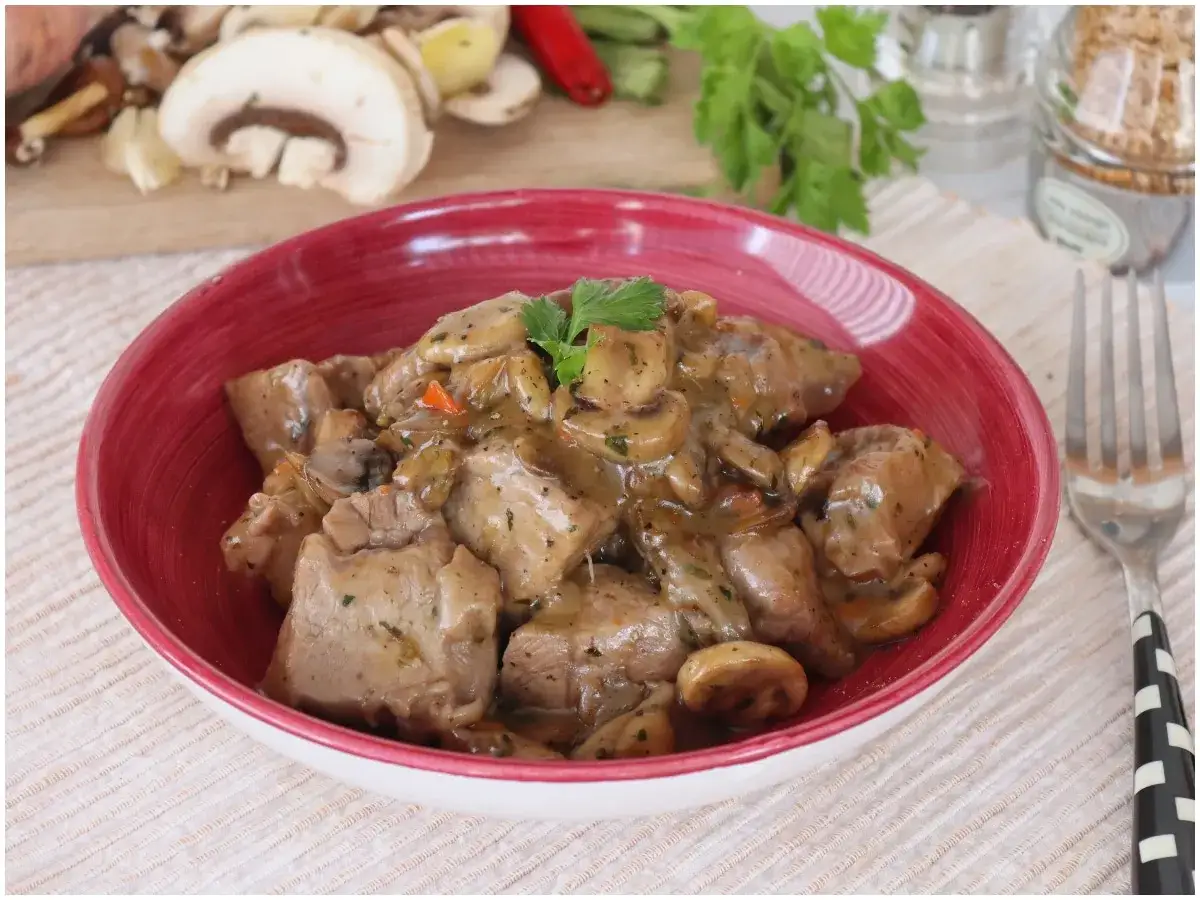 Un saporito spezzatino con funghi, servito in una ciotola rossa, pronto per essere gustato.