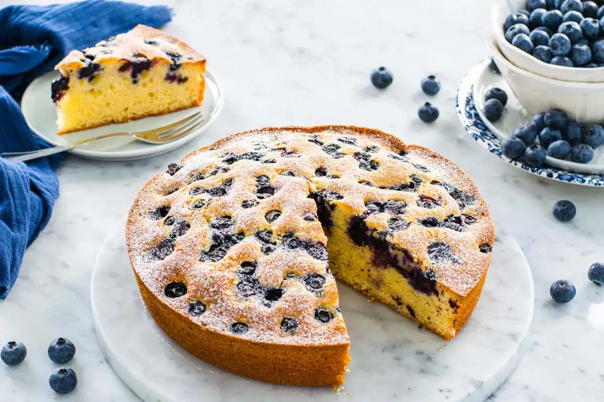 Torta 7 vasetti soffice e profumata, ricca di mirtilli e spolverata di zucchero a velo. Una fetta invitante attende di essere gustata.