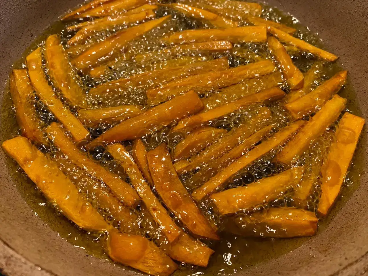Patate dolci fritte dorate che sfrigolano nell'olio caldo, pronte per essere gustate.